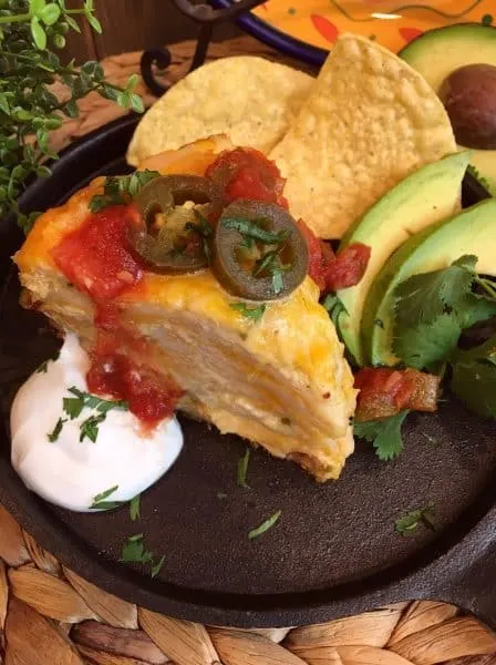 Over head shot of a thick slice of slow cooker chicken enchilada stack. Served with sour cream, salsa, jalapeno's, and tortilla chips.