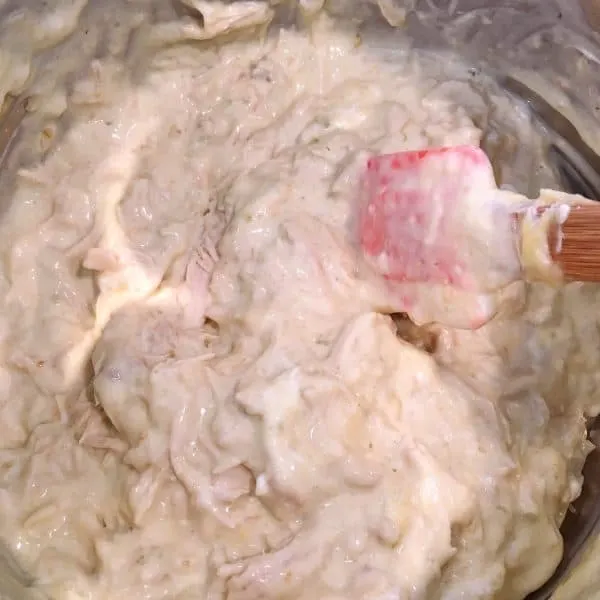 Shredded Chicken, Cream of Chicken Soup, Sour Cream, and seasonings being mixed together in a medium bowl for slow cooker stacked chicken enchiladas casserole.