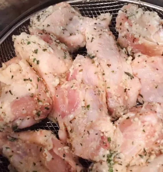 Chicken wings laying in a single layer in the fryer in the basket.