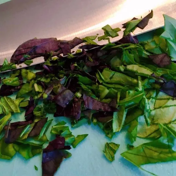 Chopped fresh basil on cutting board with a sharp knife.