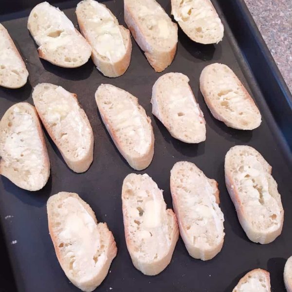 Sliced baguette buttered and on a baking sheet.