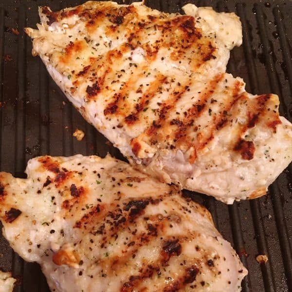 Two seasoned chicken breast grilling on stove top.