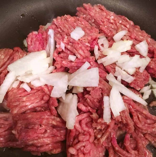Large skillet with 1 pound ground beef and diced onions over medium heat on stove.