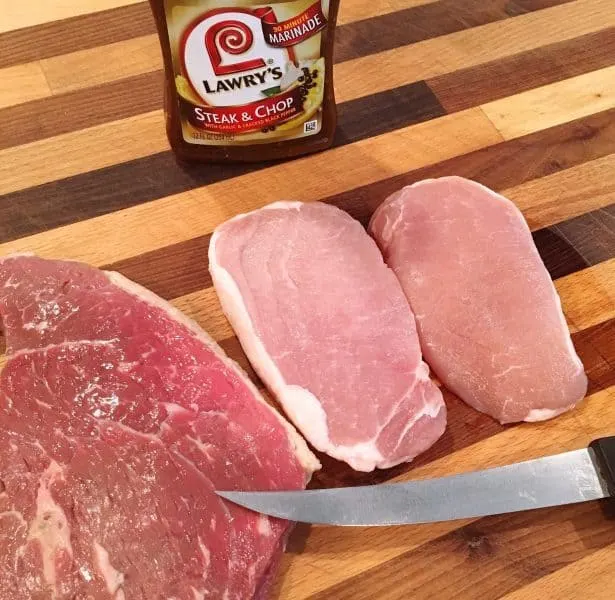 Two raw pork chops and one raw steak on cutting board
