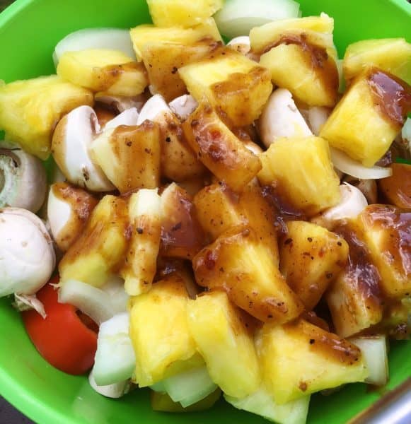 Cut up Vegetables and Pineapple in a bowl with Marinade drizzled over top