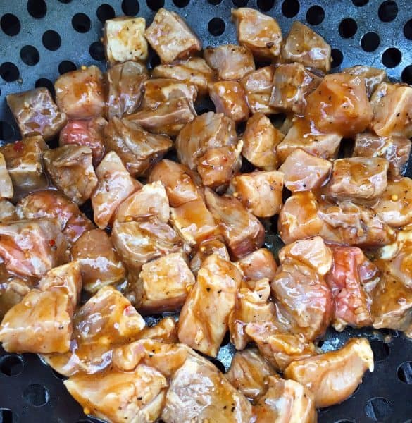 Cut up, marinated pork and steak in grilling basket over hot grill.