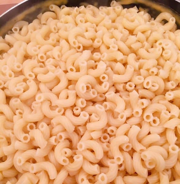Macaroni added to cheese sauce in skillet.