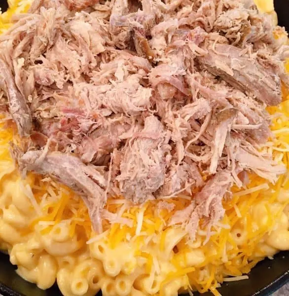 Adding shredded pork on top of macaroni and cheese