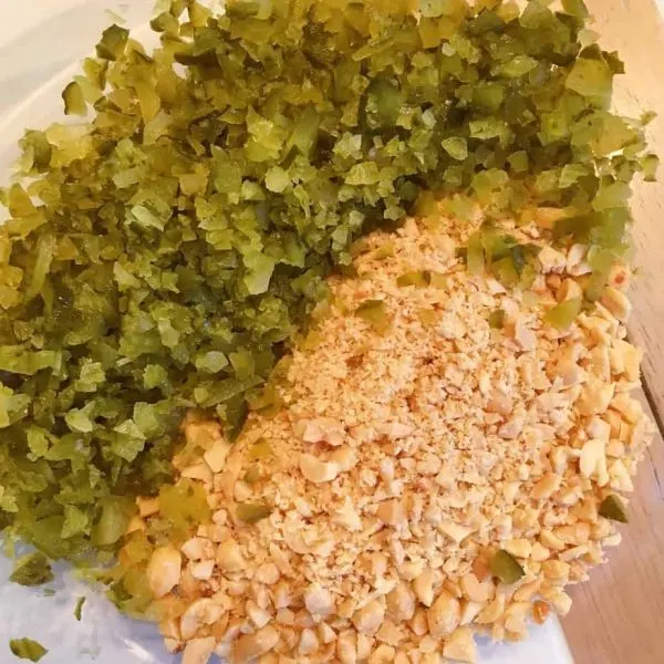 Chopped pickles and peanuts side by side in medium size bowl.