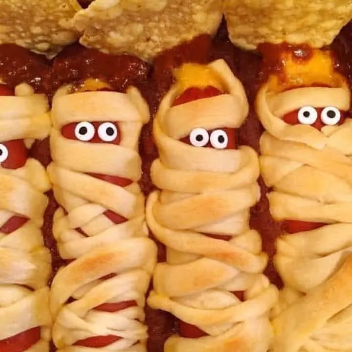 hot dogs wrapped in crescent dough strips and laid to rest in a bed of chili