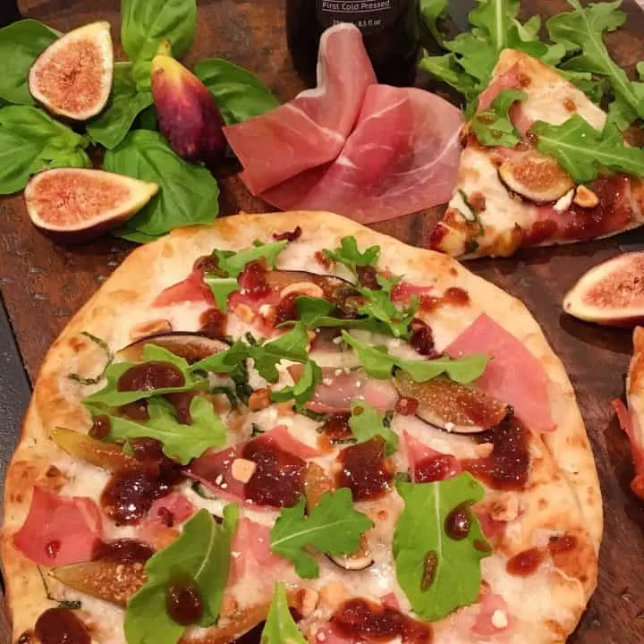 Whole Fig and Prosciutto Pizza on a board with figs and basil and cut slices of pizza