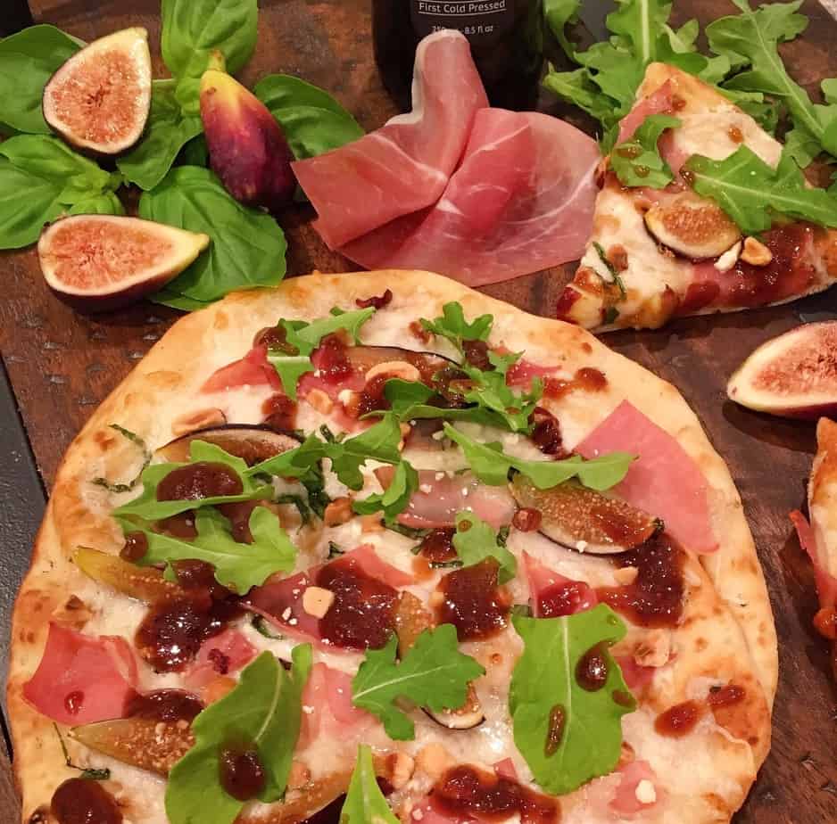 Whole Fig and Prosciutto Pizza on a board with figs and basil and cut slices of pizza