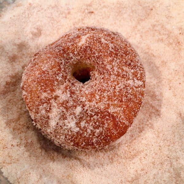 Apple Cider Donuts being rolled in cinnamon sugar