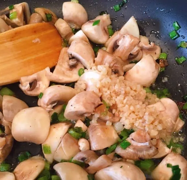 adding garlic to mushroom in skillet