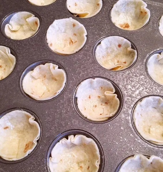 pressing tortilla circles into a muffin tin.