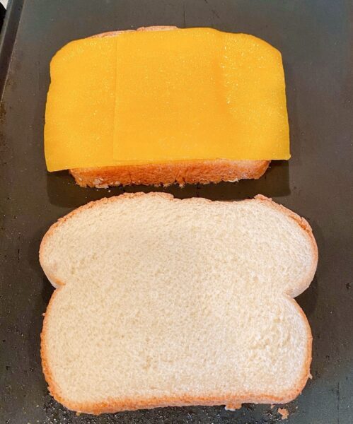 Bread on top of griddle. One slice with cheese.