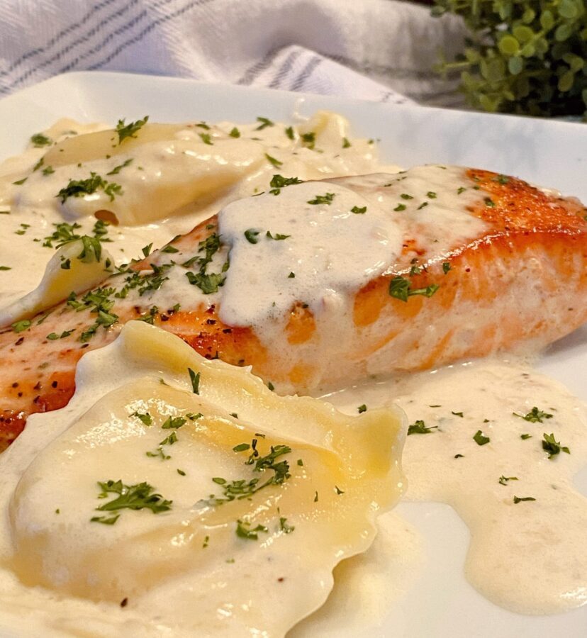 Salmon with Creamy Tuscan Sauce and lobster ravioli on a plate.