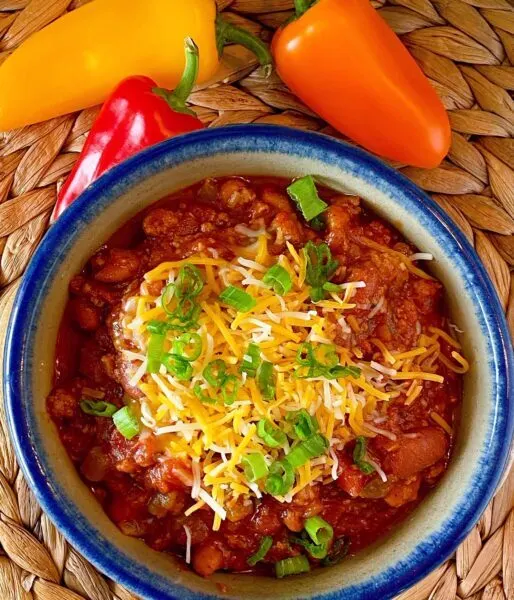 Bowl full of slow cooker chili with grated cheese and onions.