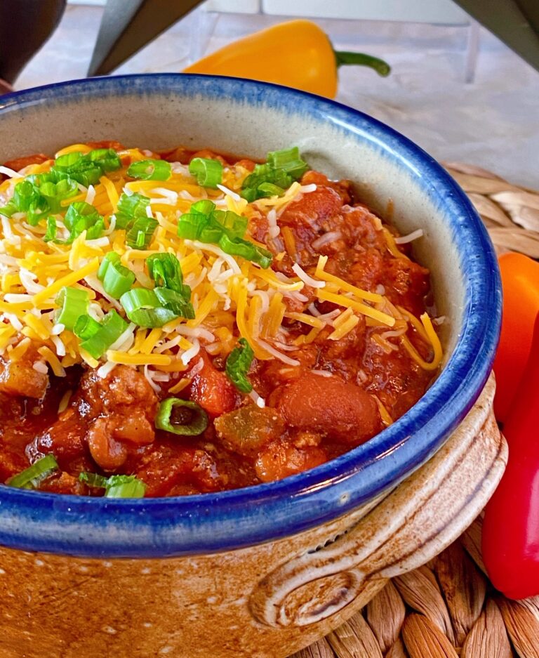 Slow Cooker Chili in a rustic ceramic bowl with cheese and green onions