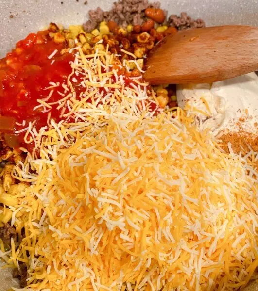 Adding two cups grated cheese and tomato sauce to casserole ingredients. Mixing it all together.