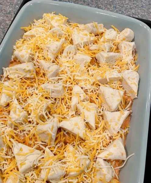 Adding grated cheese on top of the biscuits and filling for the casserole.