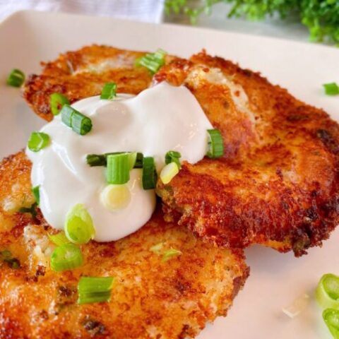 Three Loaded Mashed Potato Cakes on a plate with sour cream and chopped onions