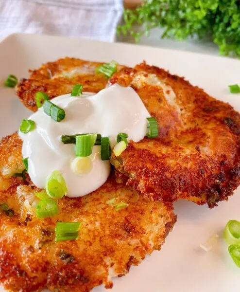 Three Loaded Mashed Potato Cakes on a plate with sour cream and chopped onions