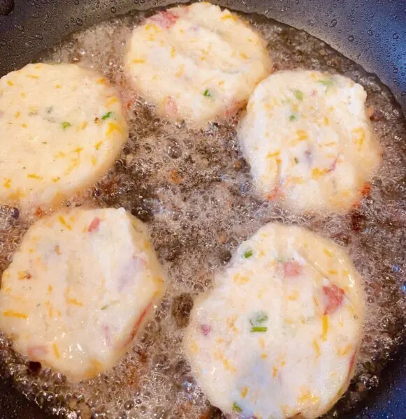 Skillet filled with hot oil and frying mashed potato patties.