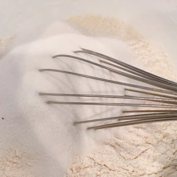 Whisking together dry muffin ingredients in a white bowl.