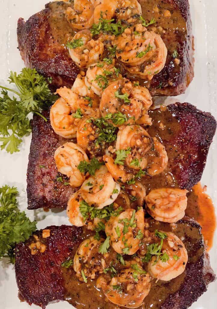Denver Steaks with Shrimp and garlic herb sauce on a platter with parsley garnish