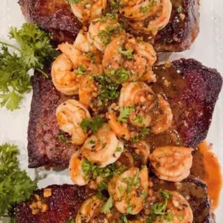 Denver Steaks with Shrimp and garlic herb sauce on a platter with parsley garnish