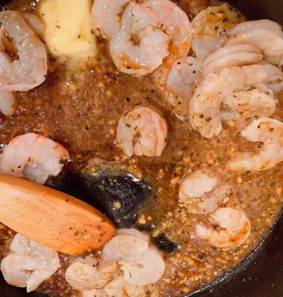 Adding garlic, butter and shrimp to hot skillet to cook the shrimp.