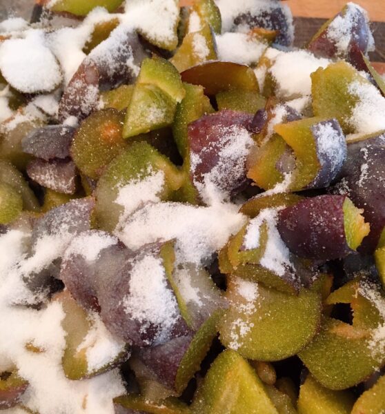 Sliced and diced purple plums with 1/2 cup sugar and lemon juice in a large bowl