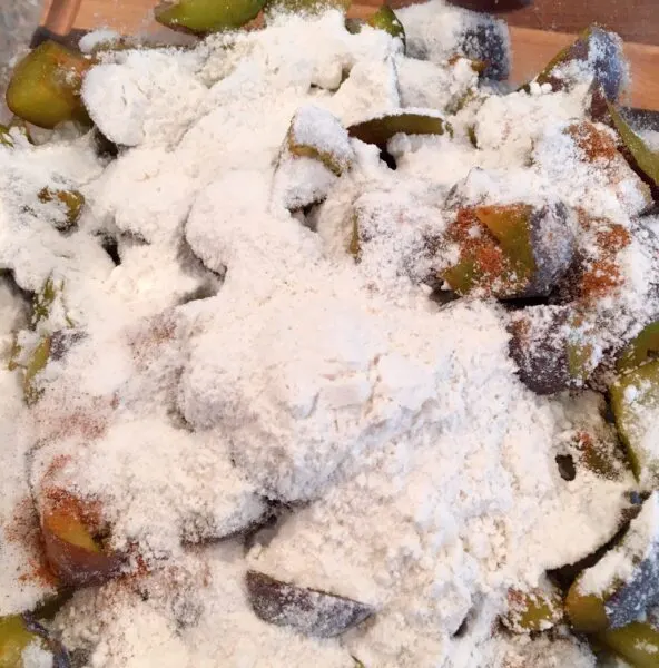 Adding flour, salt, and cinnamon to chopped plums in a bowl