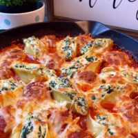 Spinach and Cheese stuffed Shells in a large cast iron skillet topped with golden brown cheese and a rich tomato sauce.