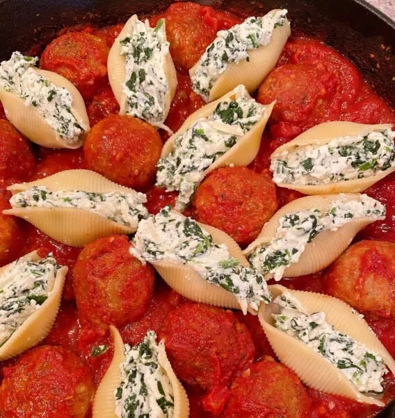 Tomato sauce and meatballs in the bottom of a cast iron skillet and stuffed shells placed in amongst them.
