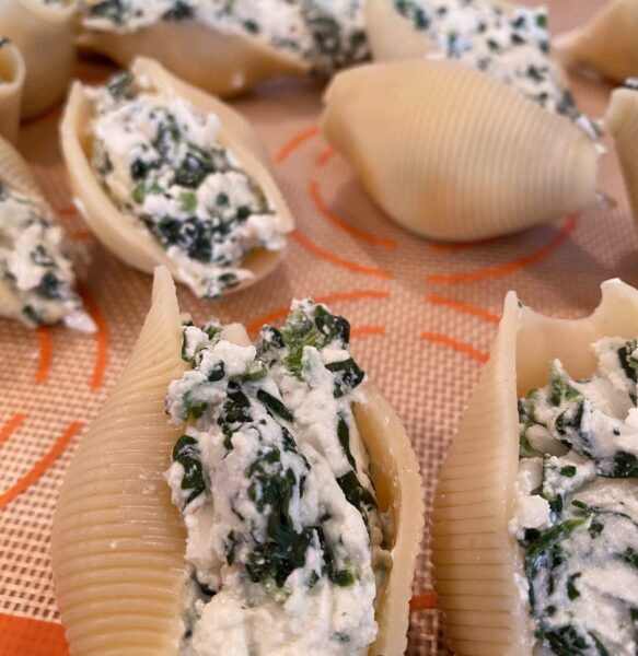 Pasta shells sitting on a baking sheet lined with a silicone baking mat, stuffed with cheese filling.