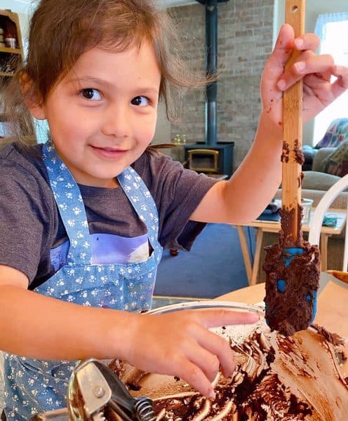 Granddaughter mixing up a batch of easy double chocolate chip cookies. Scraping off a spatula over a bowl of cookie dough.