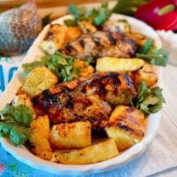 Platter filled with grilled jerk chicken breasts, grilled pineapple spears, and cilantro.