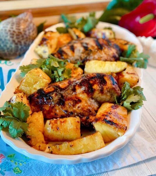 Platter filled with grilled jerk chicken breasts, grilled pineapple spears, and cilantro.