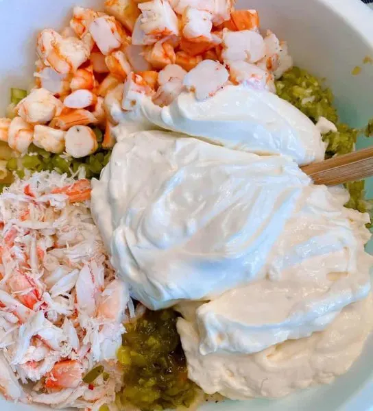 Adding Mayonnaise, sour cream, relish, and sugar to the salad mixture.