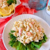 White plate with lettuce and a huge serving a Seafood Pasta Salad on a white board.