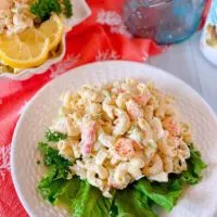 White plate with lettuce and a huge serving a Seafood Pasta Salad on a white board.