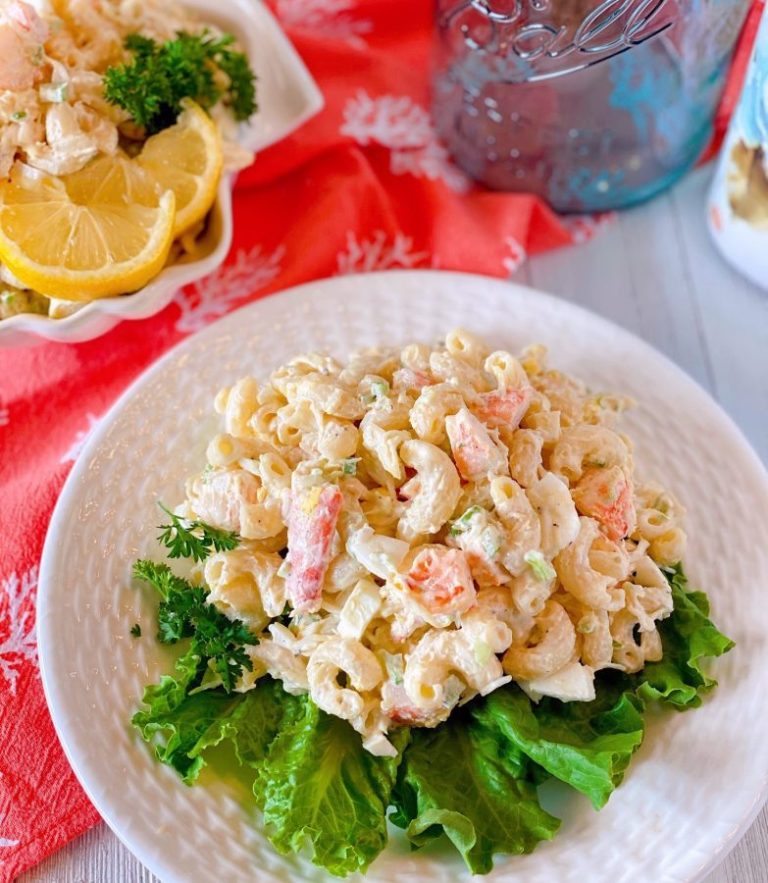 White plate with lettuce and a huge serving a Seafood Pasta Salad on a white board.