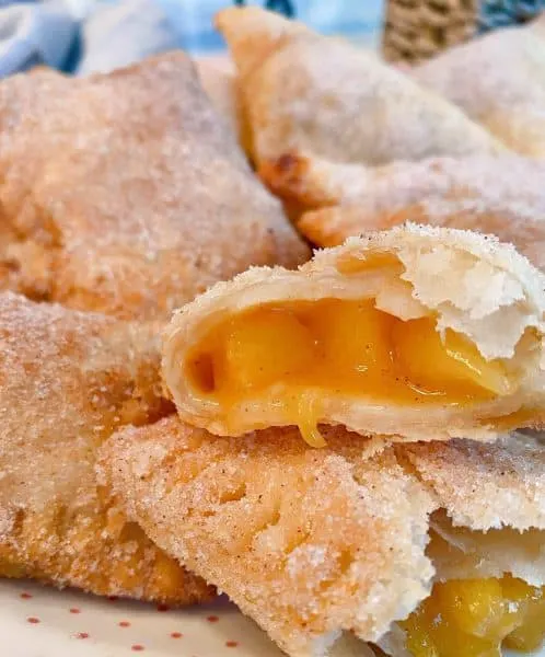 Plate of fried Peach Hand Pies with one broken open exposing the fruit filling.