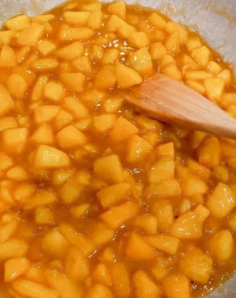 Stirring peaches in sauce to make peach pie filling for hand pies