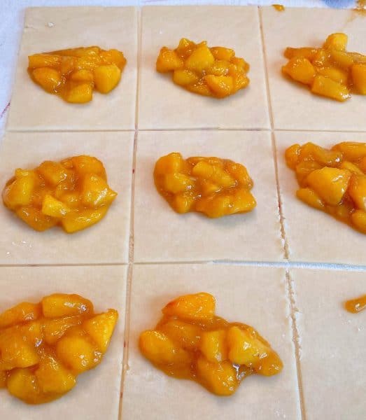 dough on flour surfaced cut into squares with peach pie filling