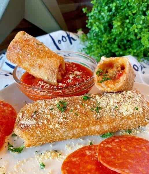 Fried Egg Rolls on a plate topped off with Parmesan Cheese and a side of marinara sauce.