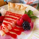 A beautiful slice of Depression Era Water Pie with raspberry sauce and fresh berries on a pretty plate.