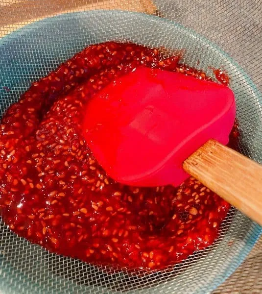 Straining raspberries and pushing down with a spatula to release all the juices.